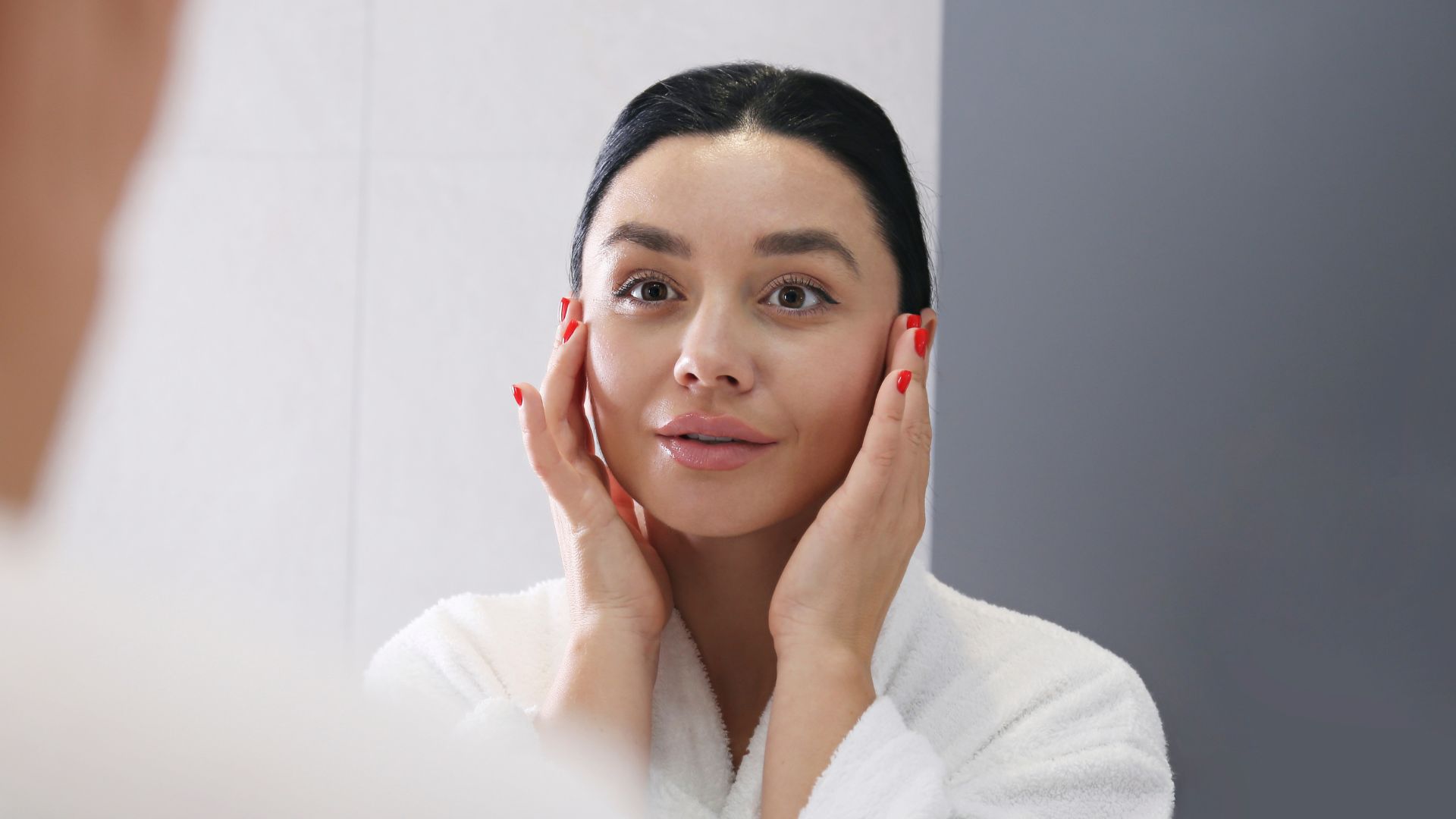 Kobieta patrząca w lustro i nakładająca serum do twarzy